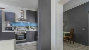 A modern kitchen with grey cabinets, a microwave, stove, and a dining area with a table and chairs. - Holiday apartment with air conditioning (Novigrad)