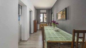 A narrow hallway leading to a dining area with a table set for four, a chair, and a vase with flowers. - Holiday apartment with air conditioning (Novigrad)