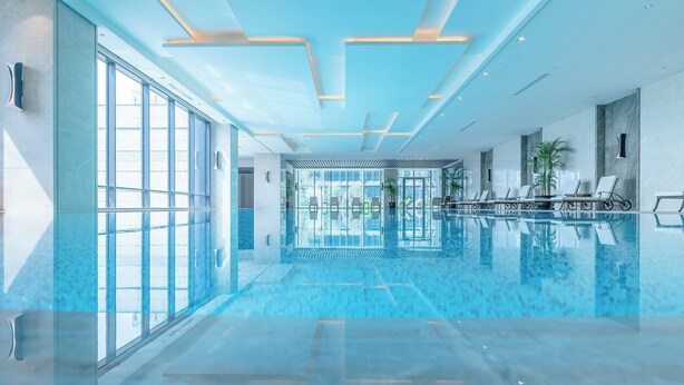 Una amplia piscina cubierta con paredes de vidrio, luces en el techo y sillones de descanso.