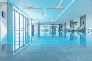 A large indoor swimming pool with glass walls, ceiling lights, and lounge chairs. - Jeurong Hotel Shanghai (Shanghai)