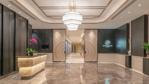 Un moderno vestíbulo de hotel con una recepción de mármol, una araña y una escalera que conduce a los pisos superiores.