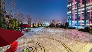Un patio con mesas al aire libre, un edificio con ventanas iluminadas y cielo despejado.