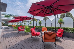 Een terras met zitplaatsen buiten, rode parasols en uitzicht op een brug.