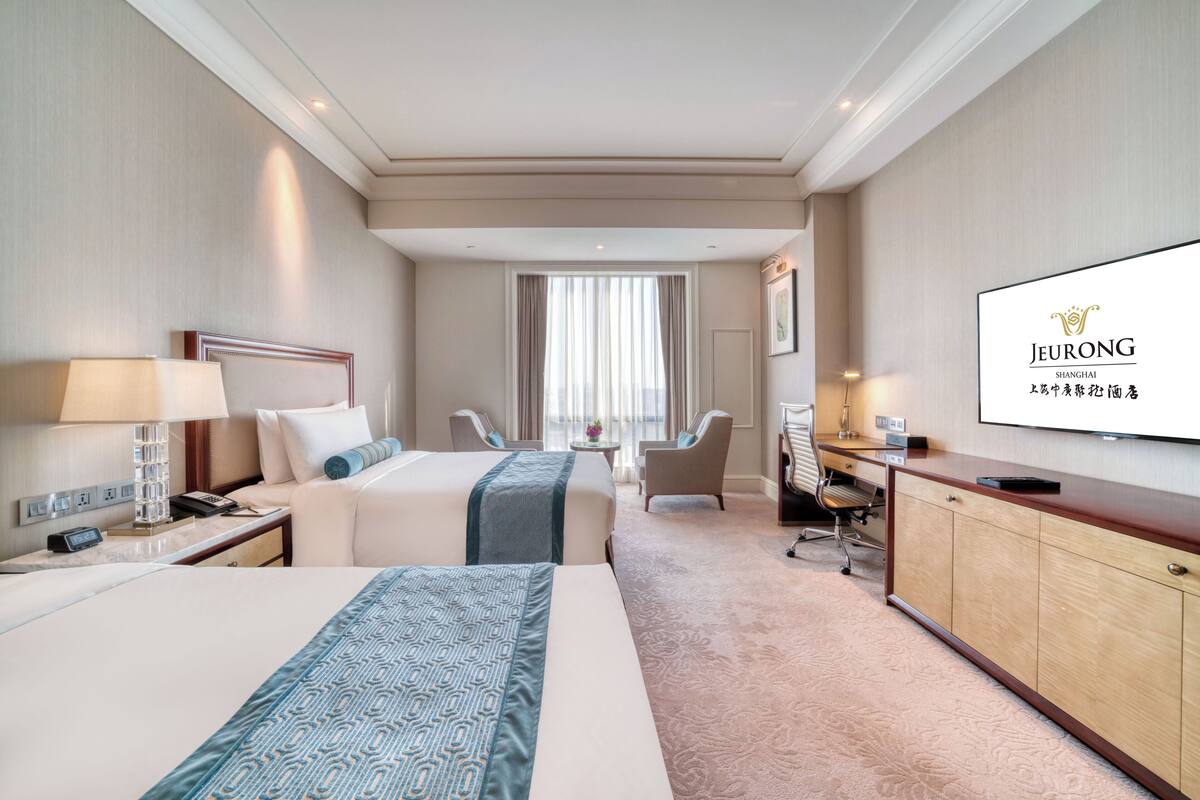 Een hotelkamer met twee bedden, een bureau, een televisie en uitzicht op de stad.