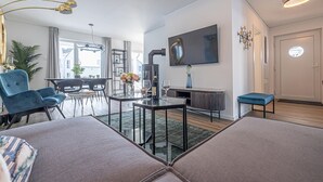 Ett modernt vardagsrum med en soffa, ett soffbord, en tv och en matplats med stolar och ett bord.
