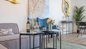 Ett modernt vardagsrum med en soffa, ett soffbord i glas, en dekorativ vas, en flaska Chianti-vin och en blå soffa.
