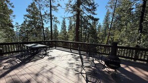 Eine Holzdielen-Terrasse mit Metallstühlen und einem Grill, umgeben von hohen Bäumen.