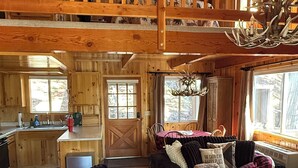 Ein Ferienhaus-Innenraum mit Holzbalkendecke, einem Essbereich, einem Wohnzimmer mit Sofa und Couchtisch sowie einer Küchenzeile.