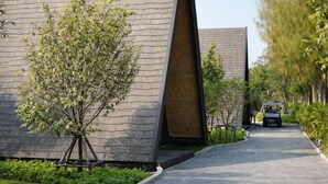 Un sendero conduce a un edificio moderno con un diseño arquitectónico singular, rodeado de vegetación y un carrito de golf.
