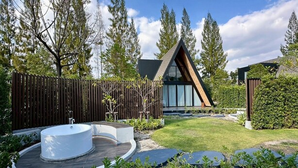 Una casa moderna con techo triangular, una terraza de madera y un gran elemento acuático en el exterior.