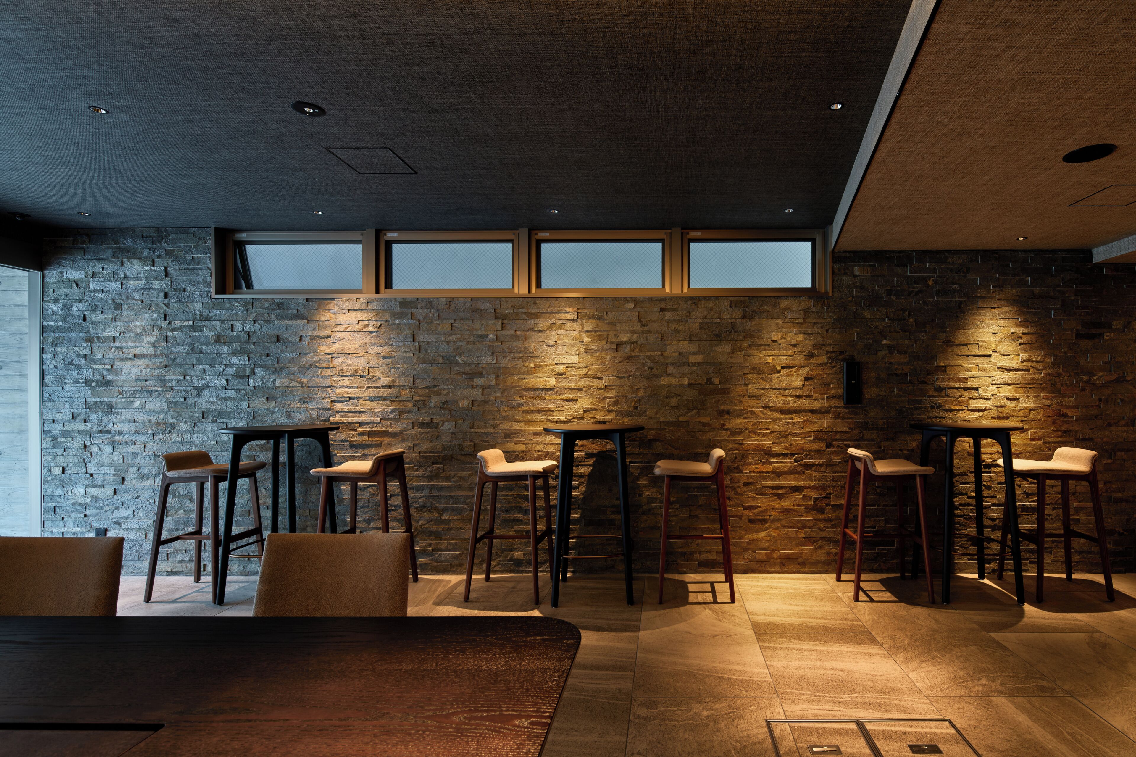 Un interior moderno con pared de piedra, varios taburetes de bar y una mesa de comedor.