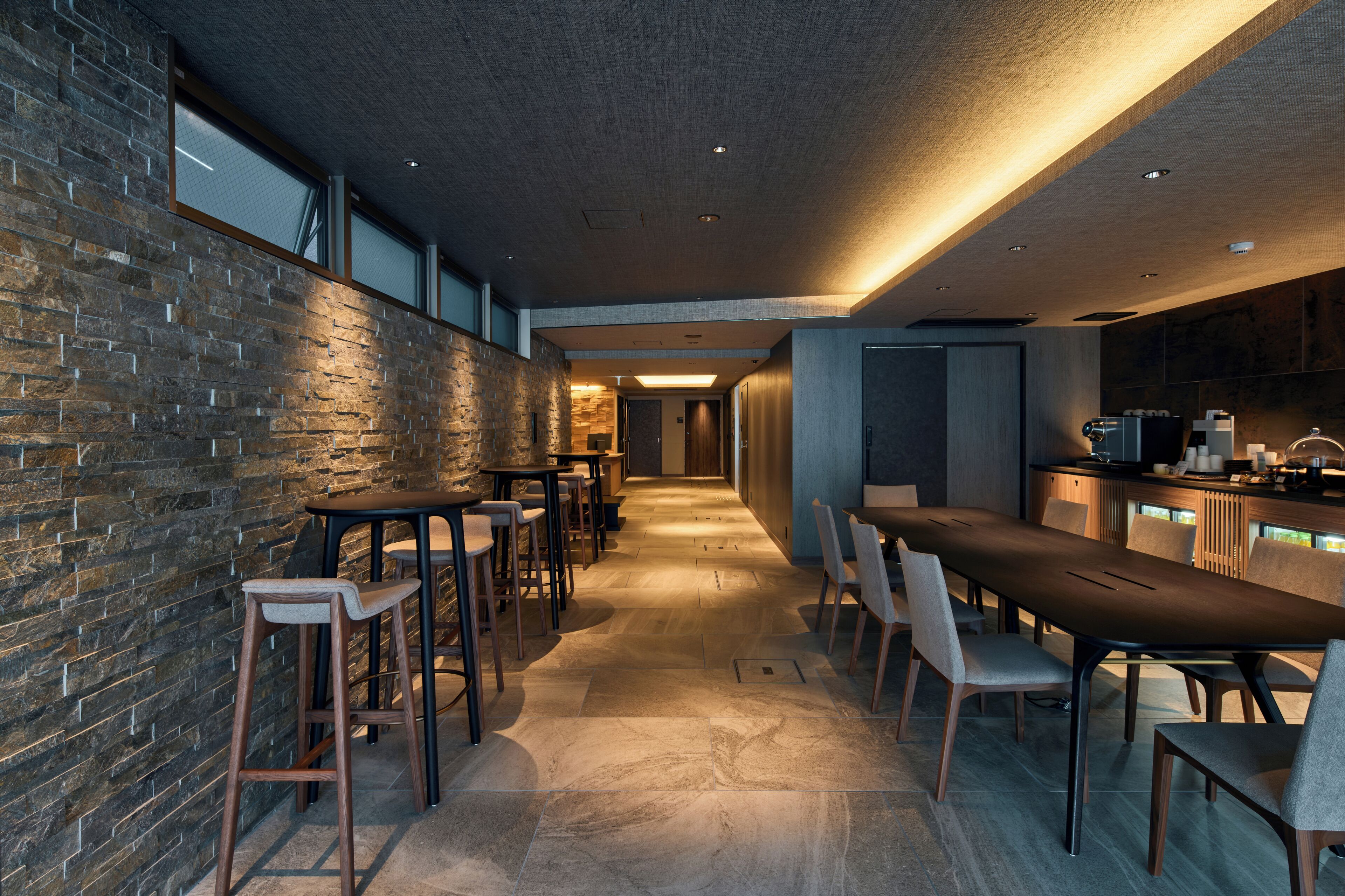 Uma área de bar moderna com um balcão comprido, banquetas e uma parede de pedra.