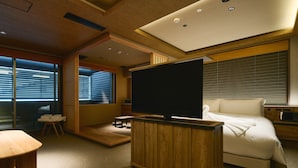 A modern hotel room with a large flat-screen TV, a bed, a seating area, and a view through large windows. - Gion Kuromatsu (Kyoto)