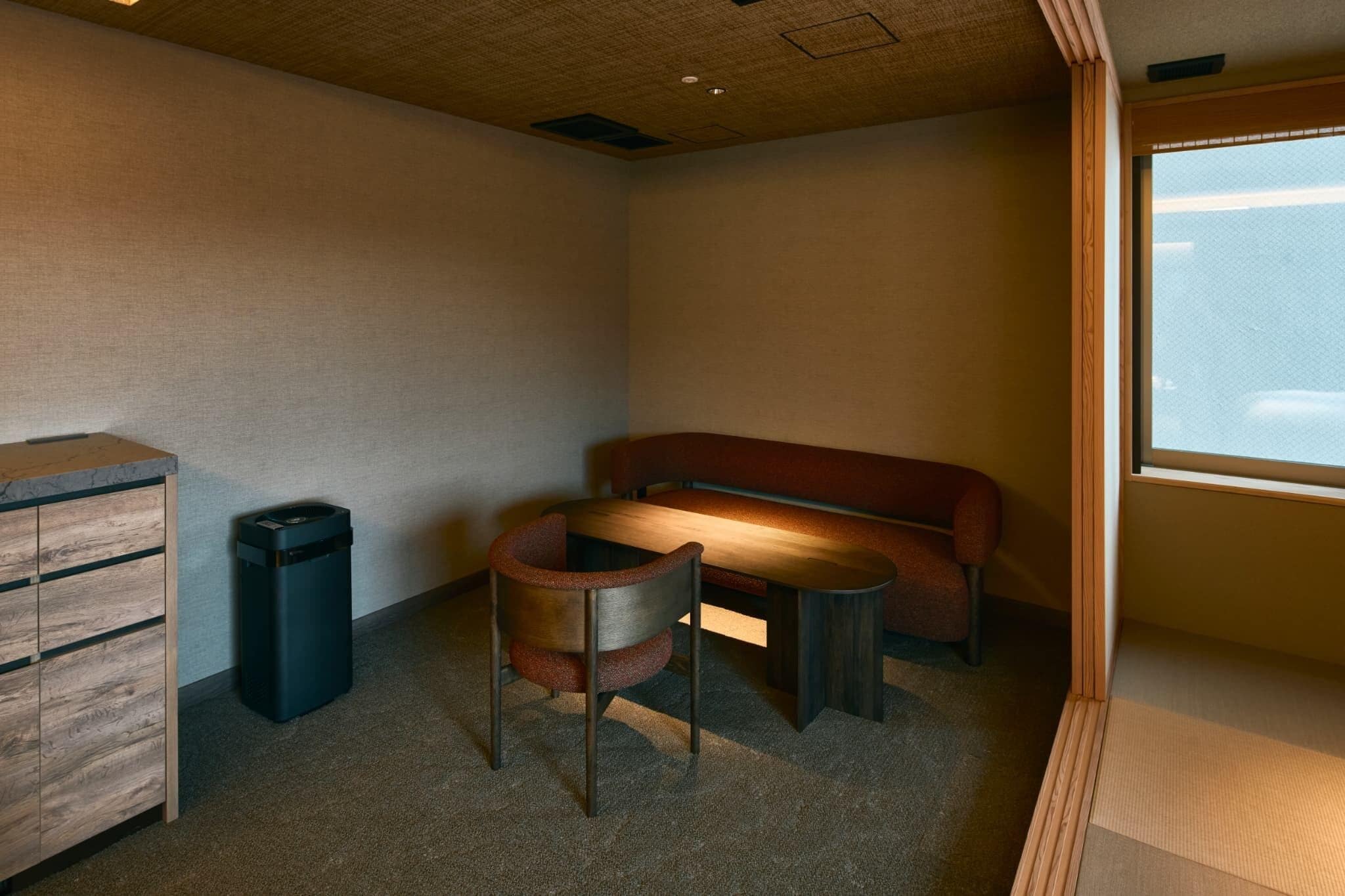 Een kamer met een houten kast, een prullenbak, een ronde stoel, een kleine tafel en een bank.