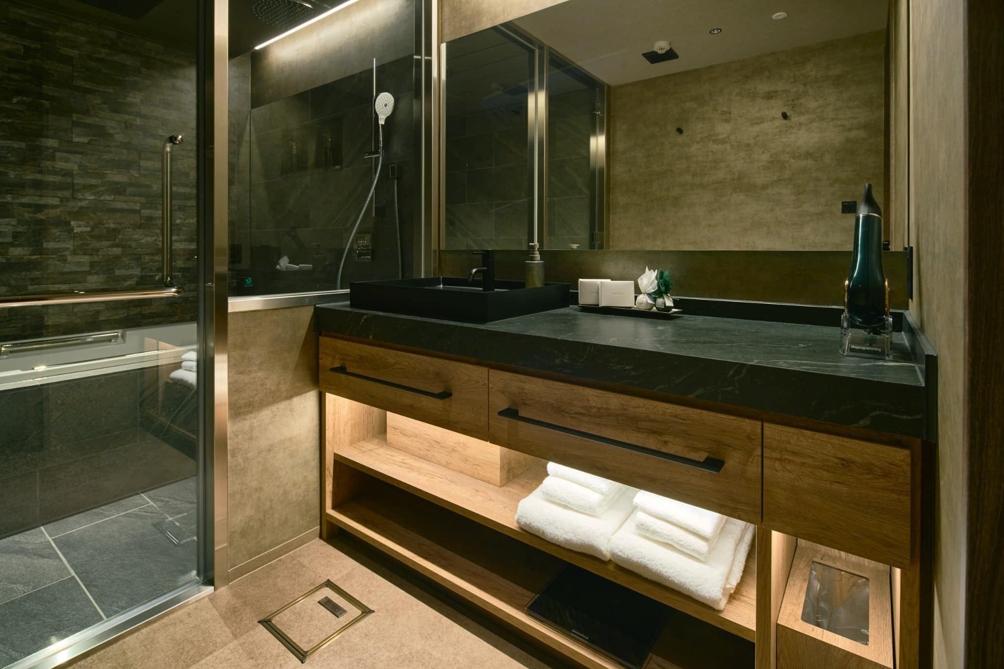 A modern bathroom with a glass-enclosed shower, a black sink, wooden vanity, and a large mirror.