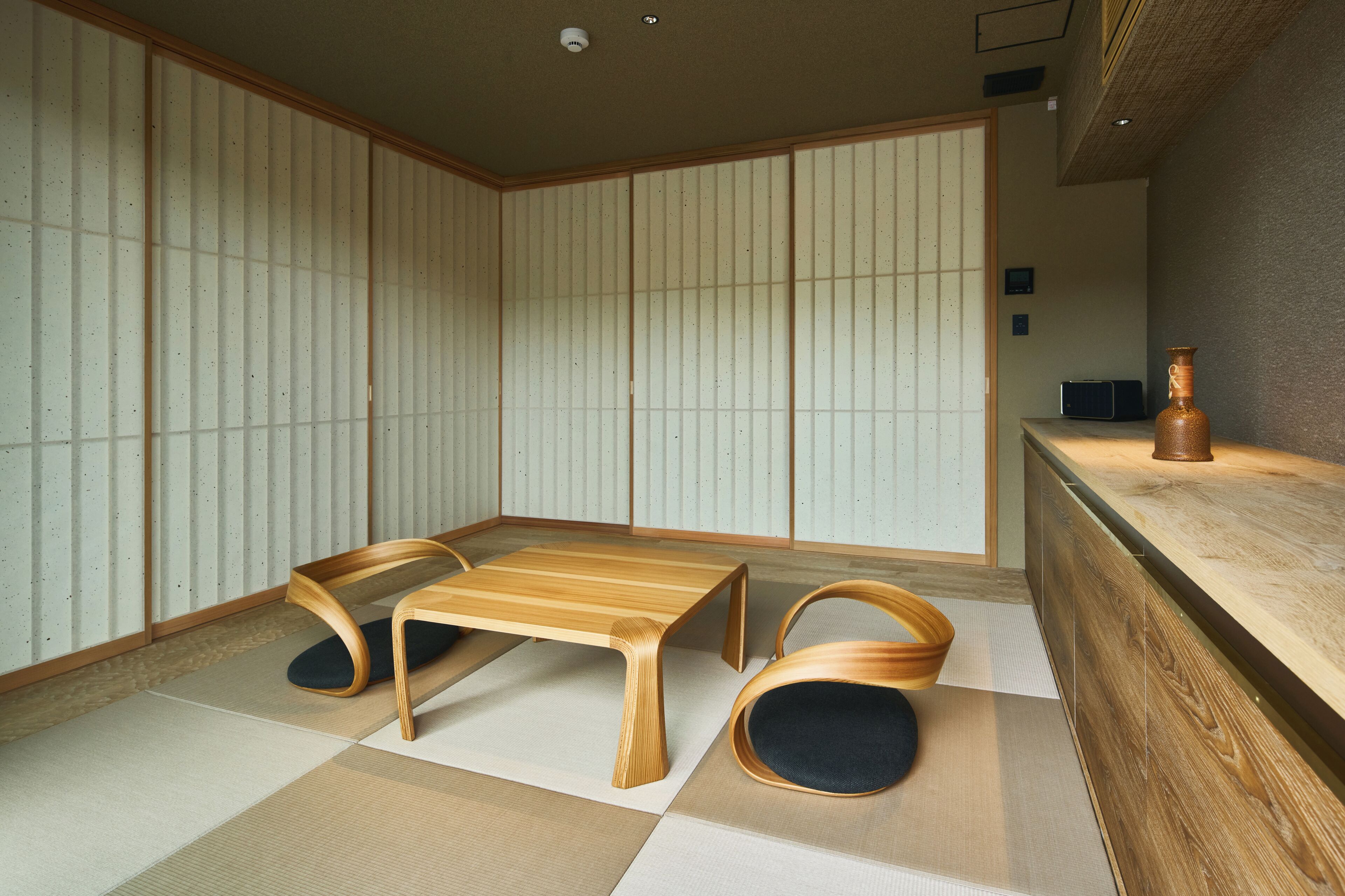 Una habitación japonesa tradicional con suelo de tatami, una mesa de madera baja y dos sillas de madera.
