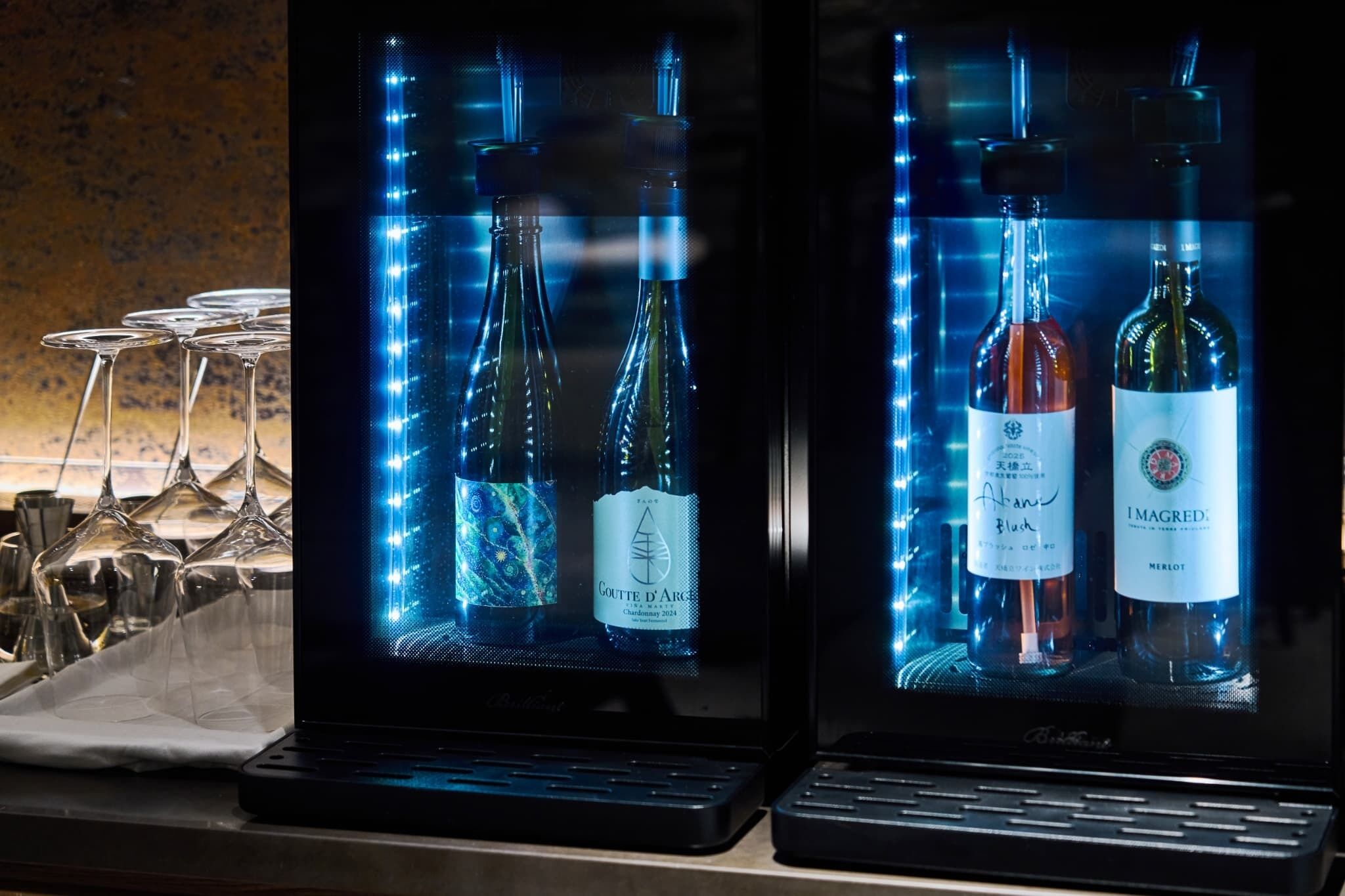 Dos refrigeradores de vino con botellas y copas sobre una encimera.