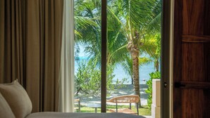 Une chambre avec un grand lit, une vue sur la mer et un palmier à l’extérieur.