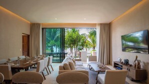 Une chambre d’hôtel moderne dotée d’un coin repas, d’un ensemble de canapés, d’une télévision et d’une grande fenêtre donnant sur un paysage verdoyant.
