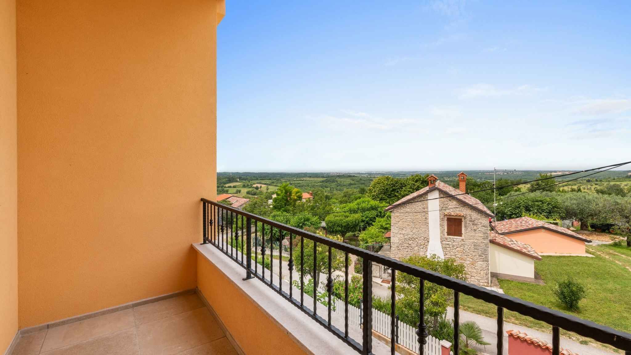 A balcony with a view of a rural landscape, stone buildings, and a clear sky.