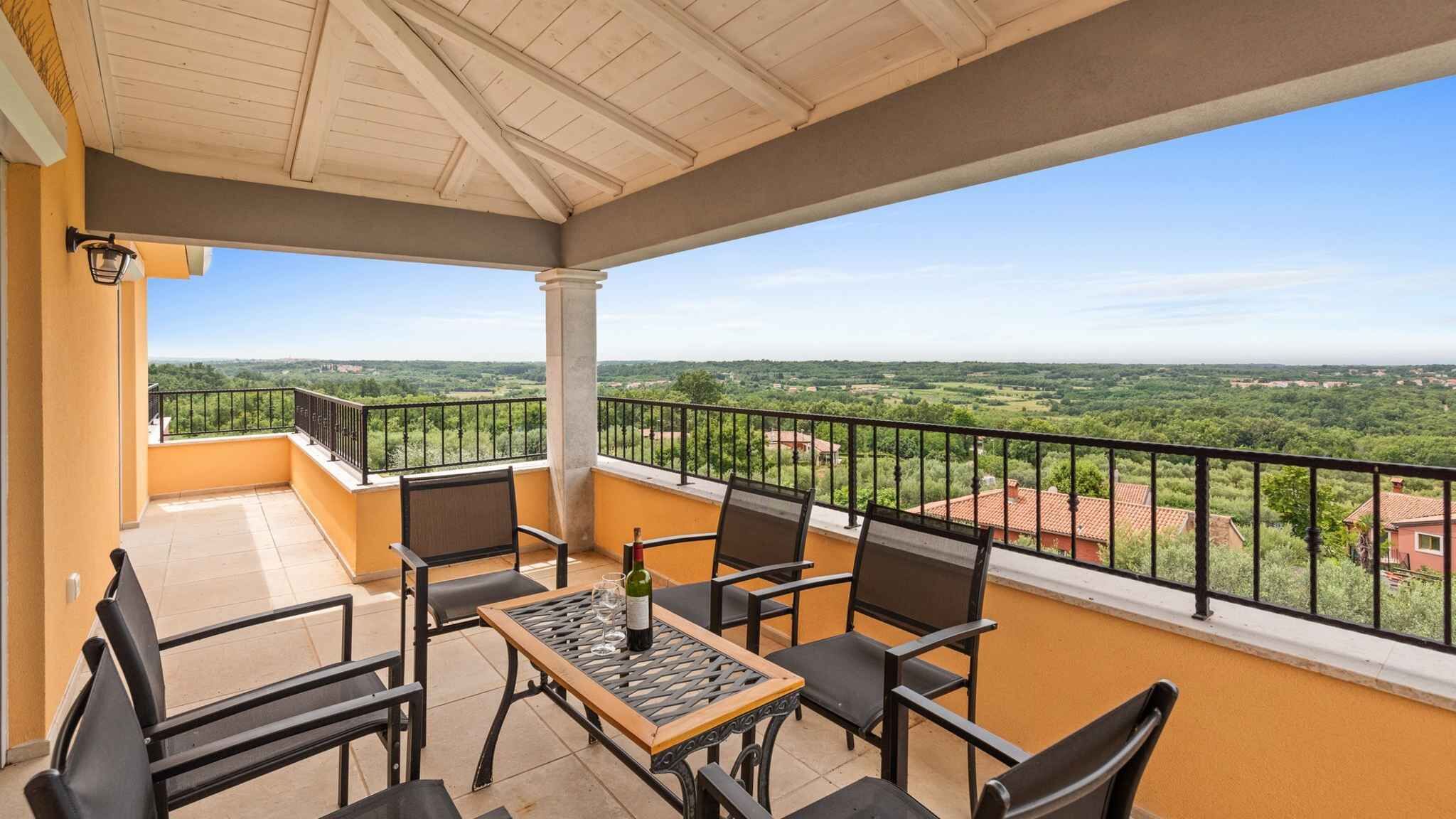 Un balcón con mesa y sillas, una botella y vistas a un paisaje verde.