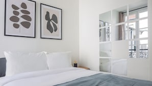 Een slaapkamer met een bed, witte kussens, een grijze deken en twee abstracte kunstwerken aan de muur.