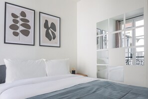 A bedroom with a bed, white pillows, a gray blanket, and two abstract art pieces on the wall. - Blueground | Plaine-Monceau, view, nr Parc Monceau (Paris)