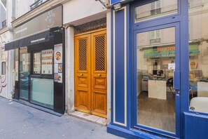 A storefront with a black awning, a wooden door with a lattice pattern, and a blue-framed window. - Blueground | Plaine-Monceau, view, nr Parc Monceau (Paris)