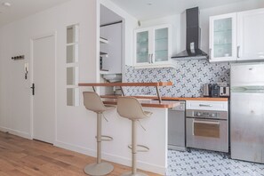 A compact kitchen with white cabinets, a stainless steel refrigerator, and a patterned backsplash. - Blueground | Plaine-Monceau, view, nr Parc Monceau (Paris)