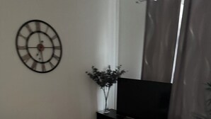 Una sala de estar con un sofá gris, una mesa de centro blanca, un mueble de entretenimiento negro y un reloj de pared.