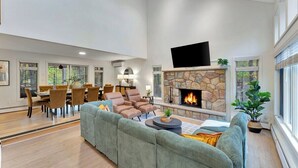 A spacious living room with a stone fireplace, a flat-screen TV, and a dining area with chairs and a table. - Unbelievable Poconos Estate - Hot Tub, Game Room (East Stroudsburg)