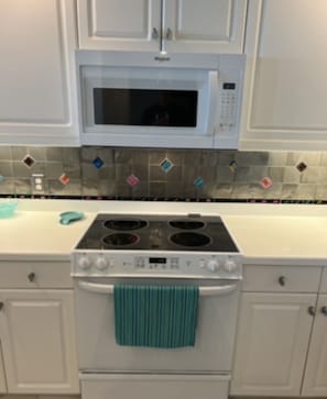 Una cocina con armarios blancos, microondas, estufa y salpicadero de azulejos.