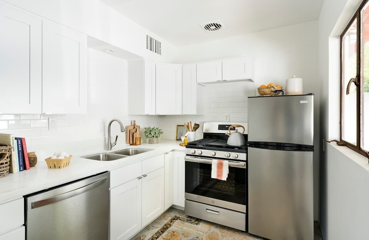 A modern kitchen with white cabinets, stainless steel appliances, a dishwasher, and a window with a view.