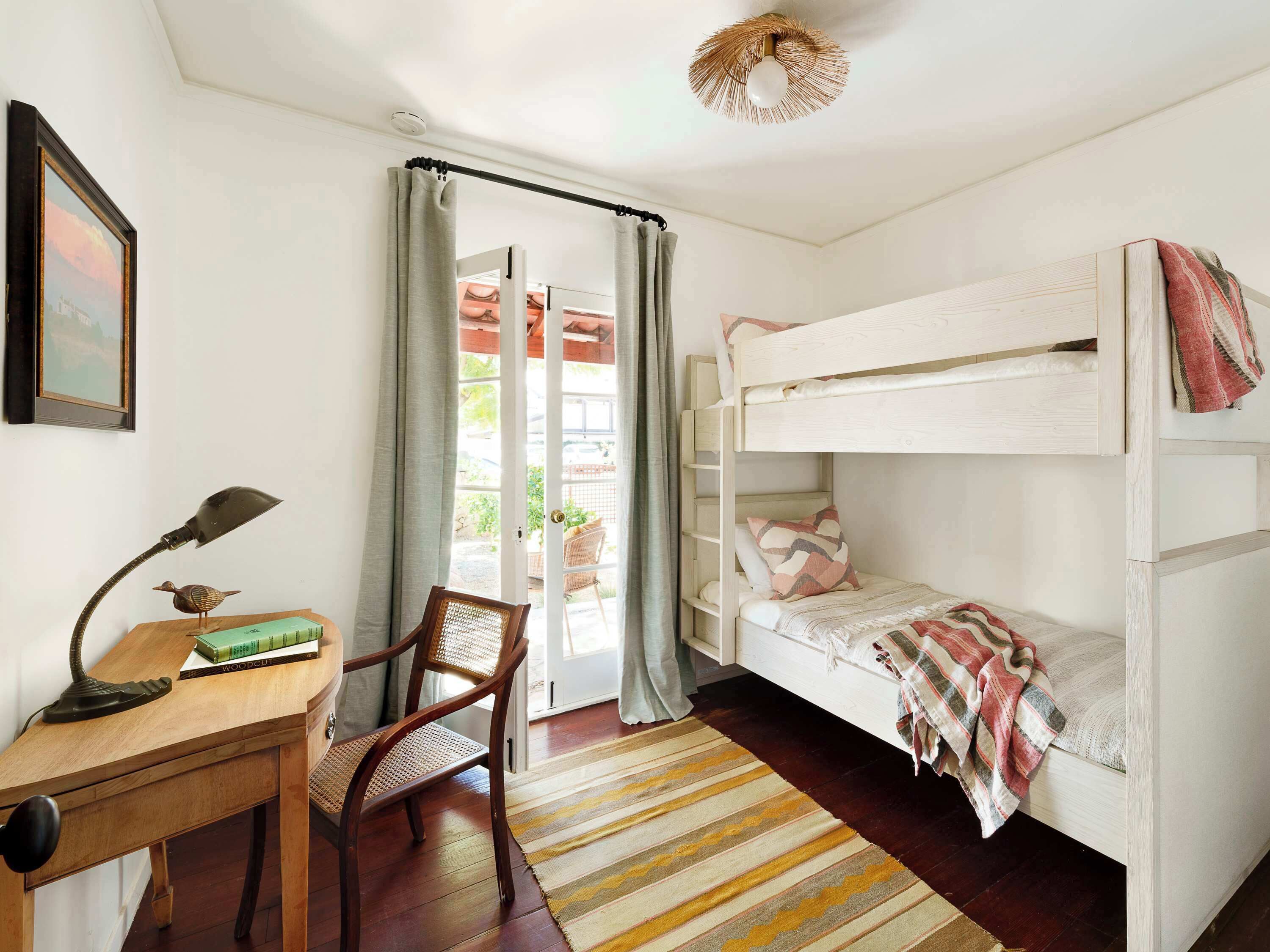 A room with a bunk bed, a desk with a lamp, a chair, and a door leading outside.