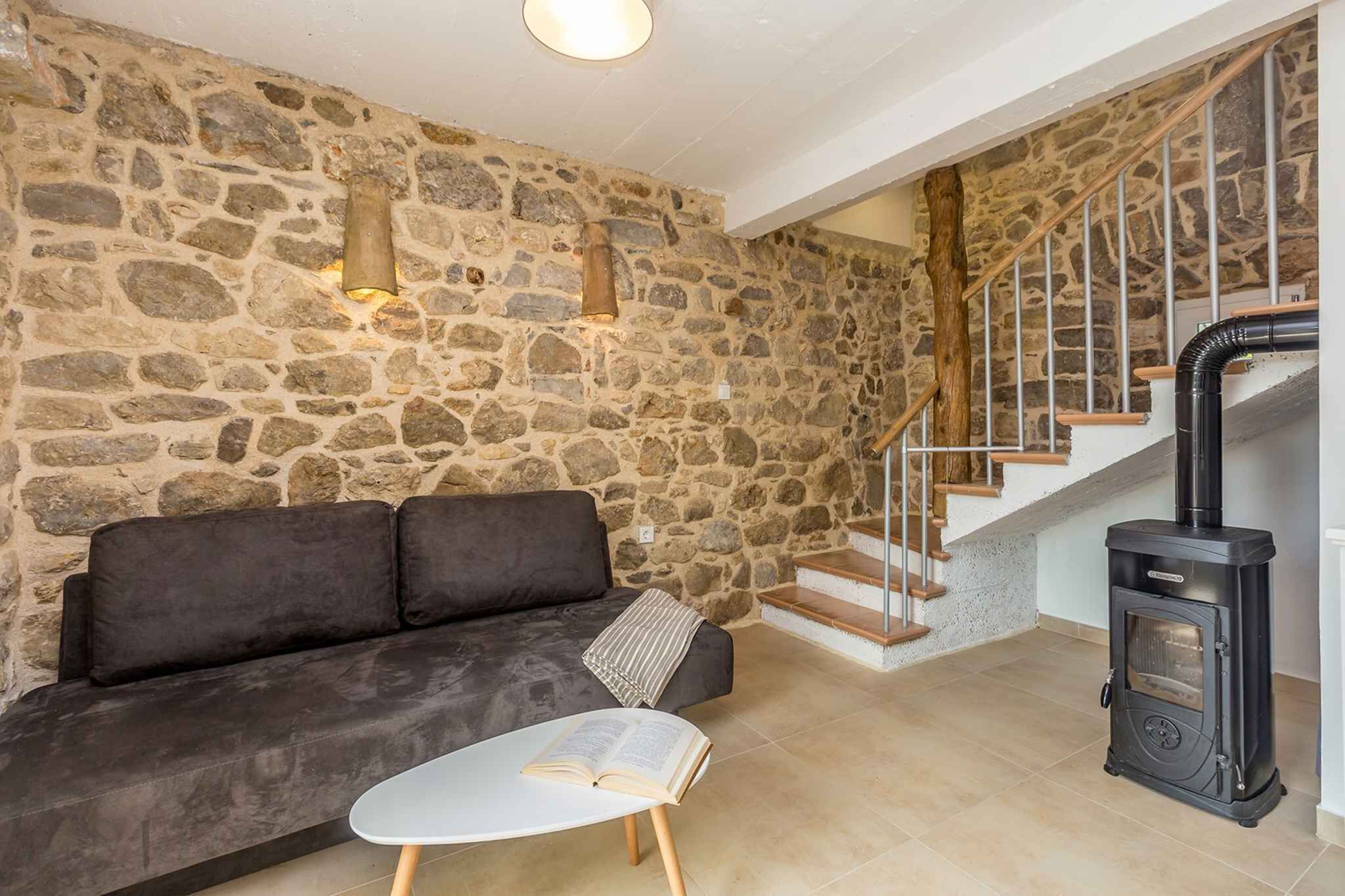 A stone-walled room with a sofa, a table with a book, a black wood-burning stove, and a staircase.