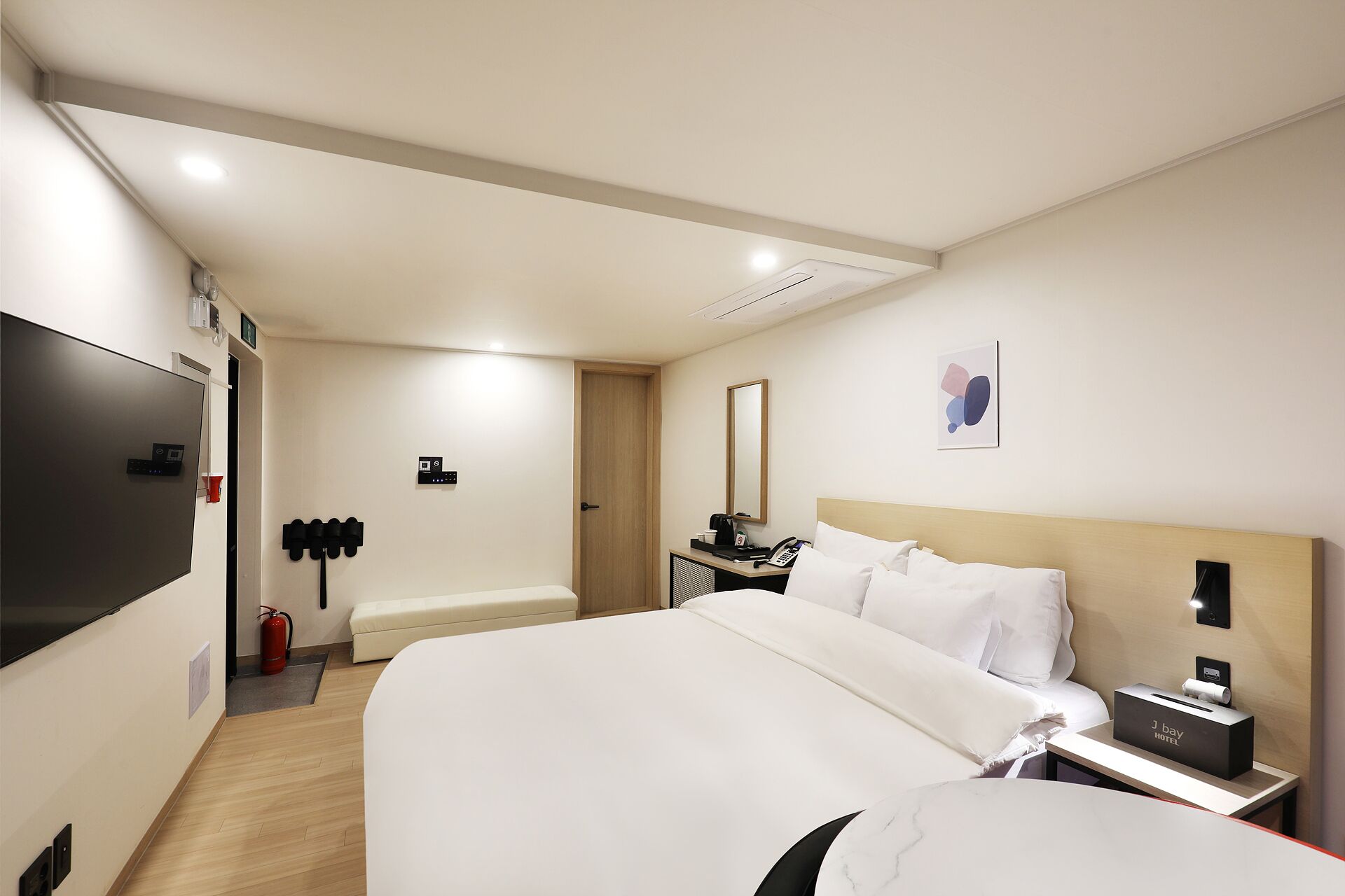 Habitación de hotel con cama, mesita de noche, espejo y televisión montada en la pared.