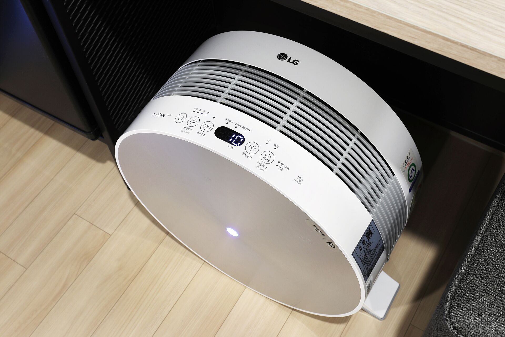 A white LG air purifier with a digital display and control panel, placed on a wooden floor.