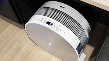 A white LG air purifier with a digital display and control panel, placed on a wooden floor.