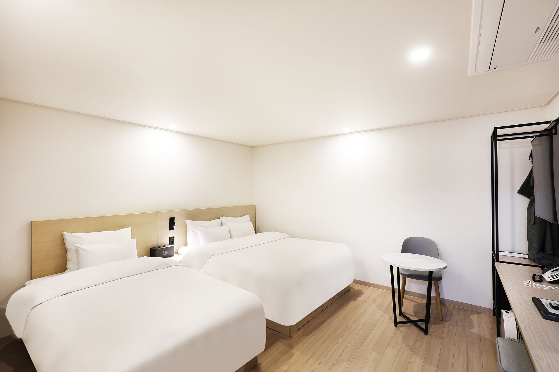 Habitación de hotel con dos camas, una mesita, una silla, un escritorio con teléfono y un espejo.