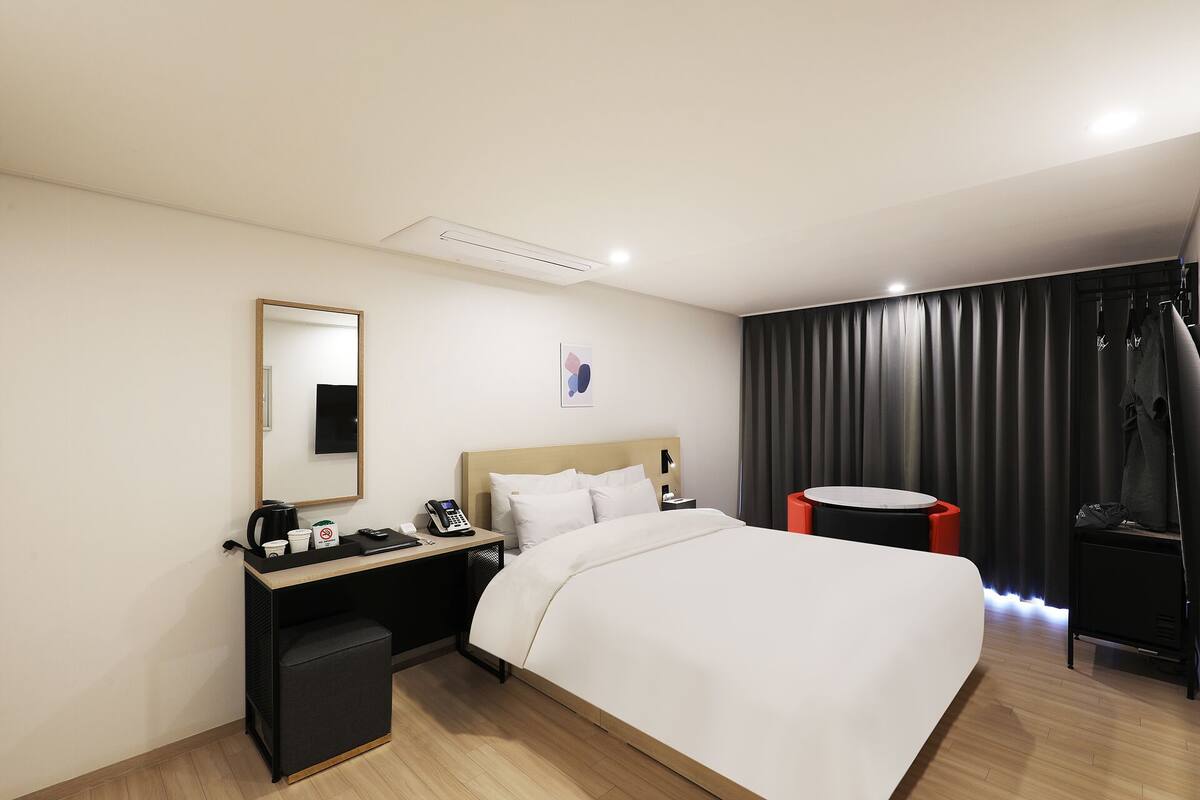 Een hotelkamer met een bed, nachtkastje, spiegel en een klein rond tafeltje met een stoel.