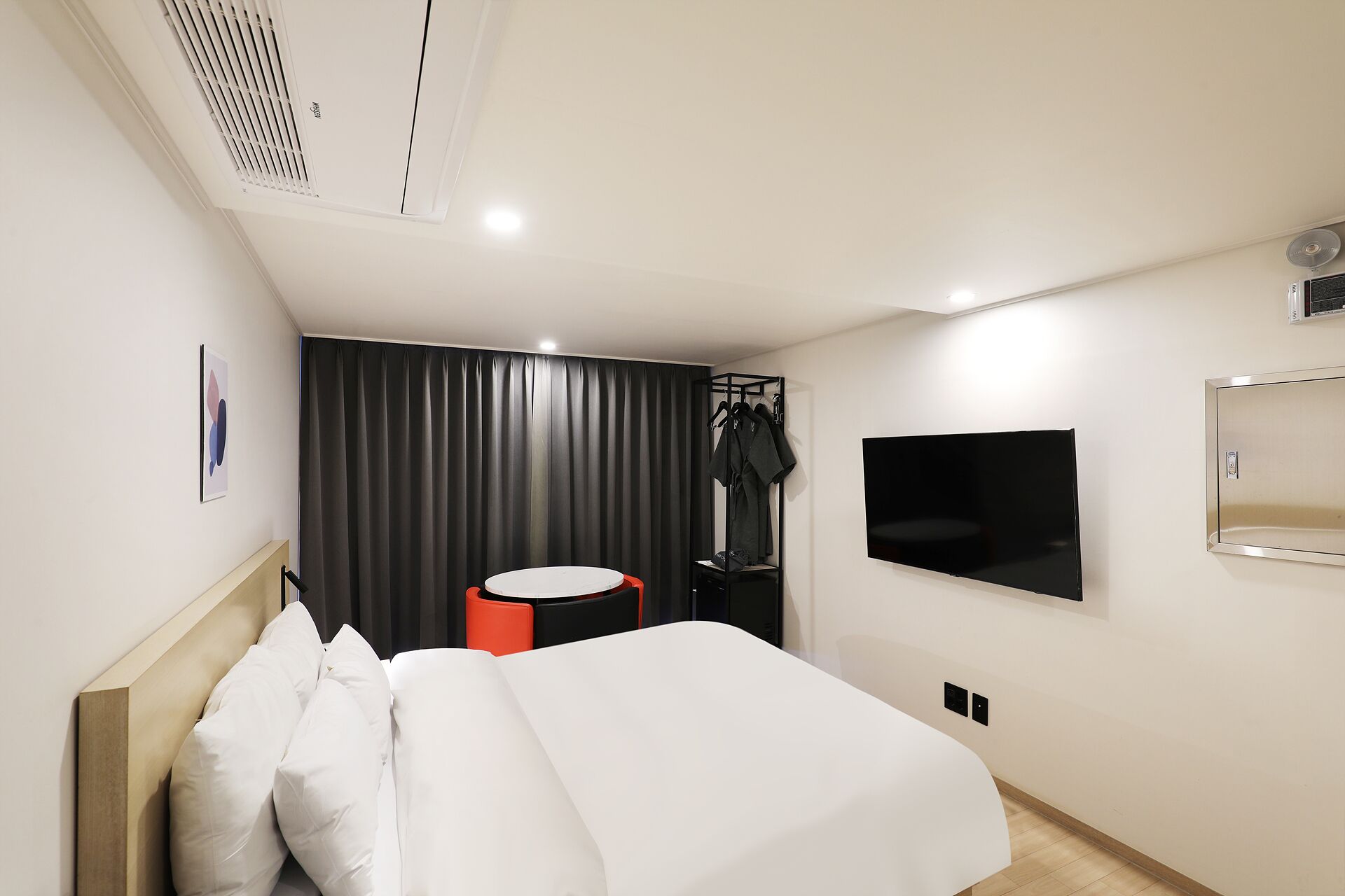 A modern hotel room with a bed, a TV, a coat rack, and a window with curtains.