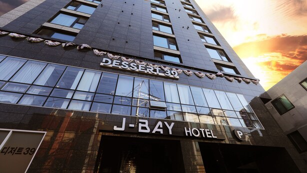 Un bâtiment moderne avec une enseigne indiquant « Dessert 39 » et « J-BAY HOTEL », ce qui laisse supposer qu’il s’agit d’un hôtel et peut-être aussi d’une boutique de desserts.