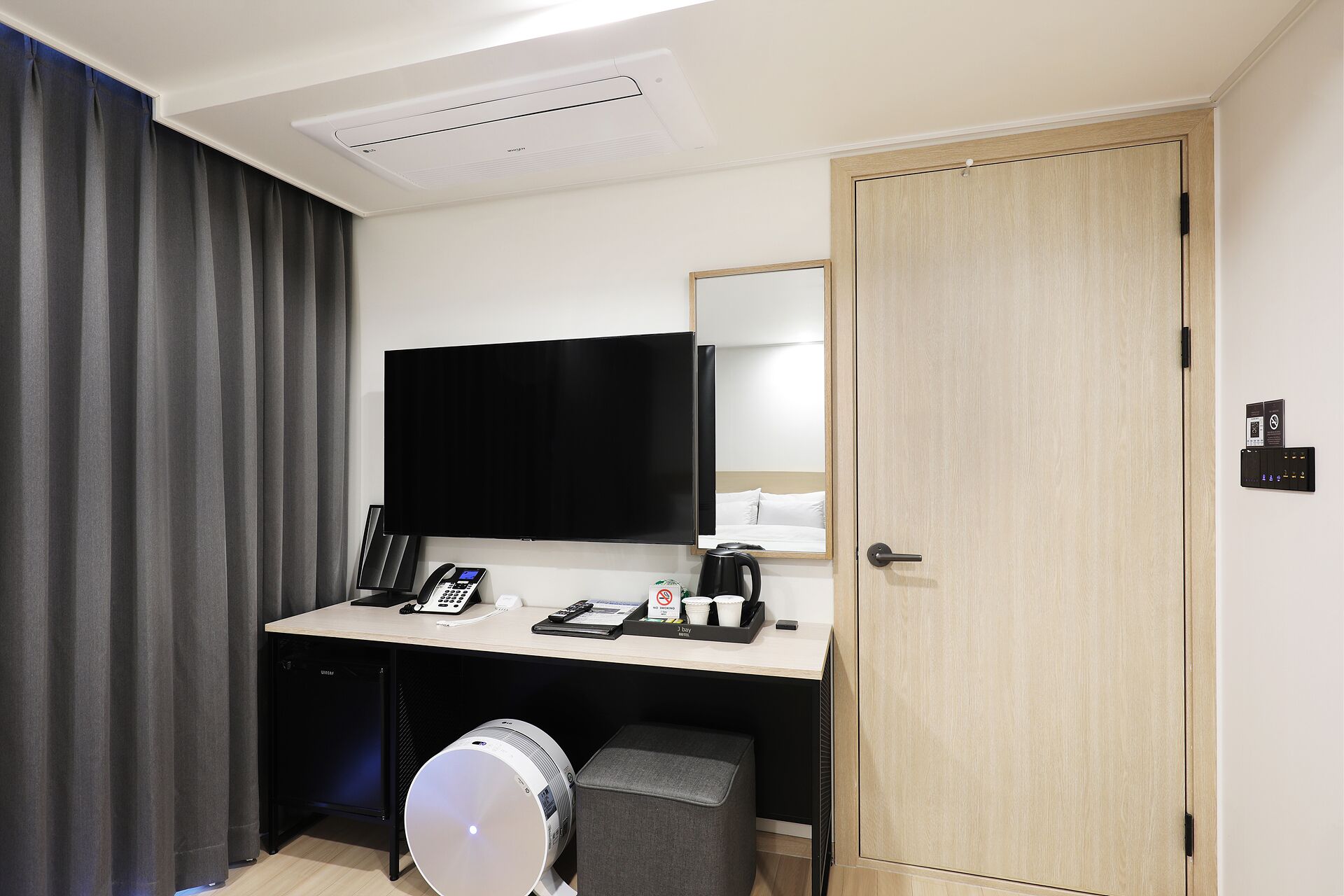 Quarto de hotel com escrivaninha, televisão de tela plana, cafeteira, telefone e um pequeno banquinho.