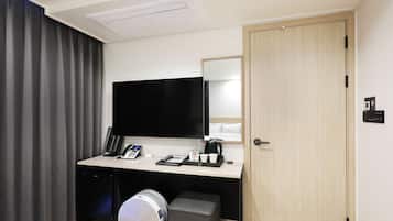 Quarto de hotel com escrivaninha, televisão de tela plana, cafeteira, telefone e um pequeno banquinho.