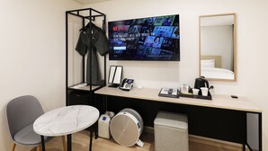Une chambre d’hôtel équipée d’un bureau, d’une chaise, d’un téléviseur diffusant un film, d’un miroir et d’un porte-manteau.