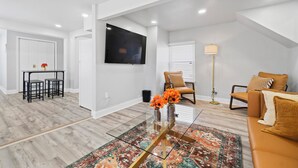 A modern living room with a glass coffee table, a sofa, a TV, and a dining area with chairs. - Cozy 4 Bed 2 Bath Home - Norfolk, Centrally Located (Norfolk)