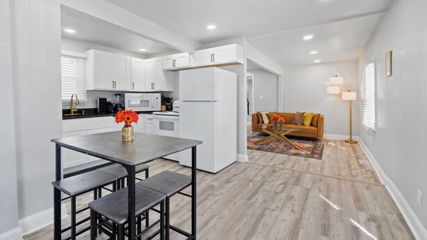 A modern kitchen with white cabinets, a dining table with benches, a refrigerator, and a sofa in the adjacent living area. - Cozy 4 Bed 2 Bath Home - Norfolk, Centrally Located (Norfolk)