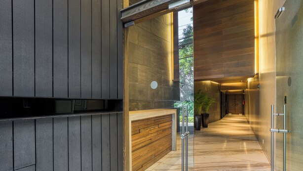 A modern interior with a wooden reception desk, a glass partition, and a hallway leading to a door. - Chic Barrio Living in Roma Norte - 2BR & Rooftop (Ciudad de México)
