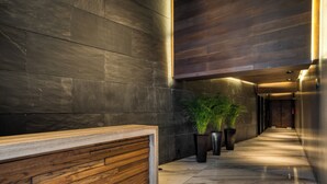 A modern reception area with a wooden reception desk, dark stone walls, and potted plants. - Chic Barrio Living in Roma Norte - 2BR & Rooftop (Ciudad de México)