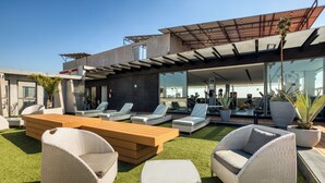 A rooftop lounge with outdoor seating, a modern building, and a clear sky. - Chic Barrio Living in Roma Norte - 2BR & Rooftop (Ciudad de México)